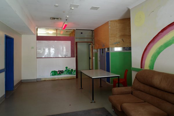 Colour photograph showing interior of a lounge area, with rainbow painted on the wall, couch and table.